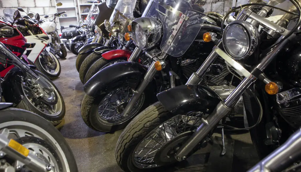 Rows of cruiser and sport motorcycles parked side by side in an indoor motorcycle storage facility