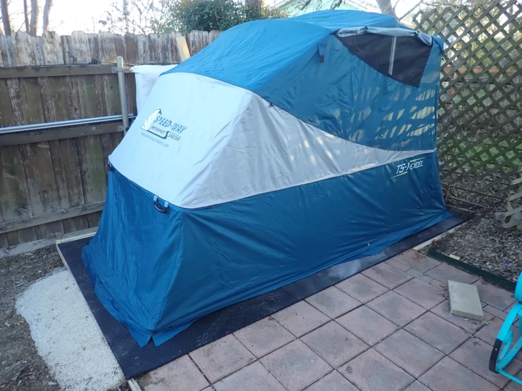 Speedway Shelter closed on a rubber floor on a paver patio along a wood fence
