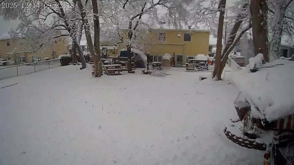 Snowy backyard security-camera view with a Touring Speedway Shelter at the right edge